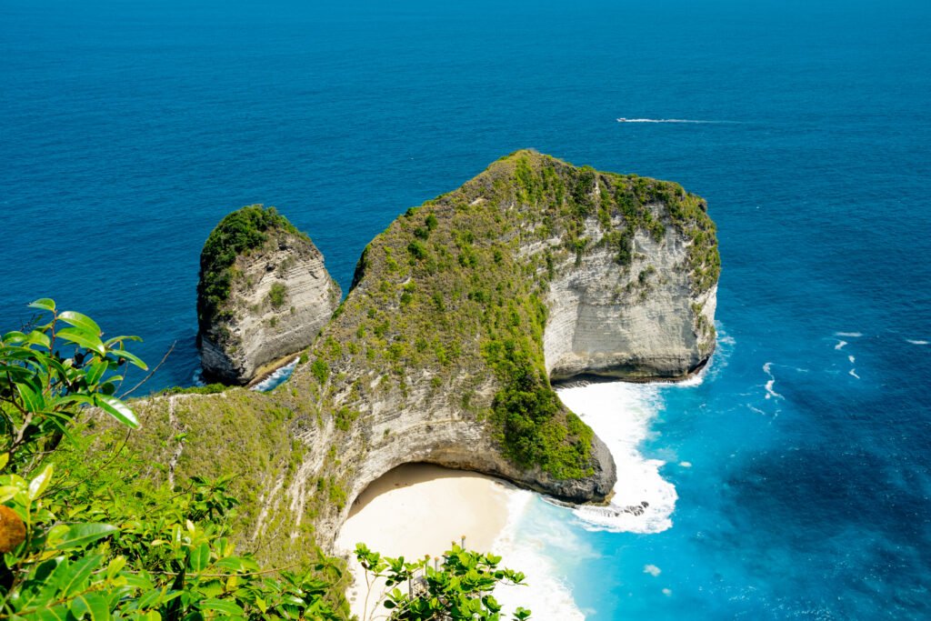 The dinosaur shaped cliff called Kelingking cliff stands firm covered with green lush and surrounded by clear blue water